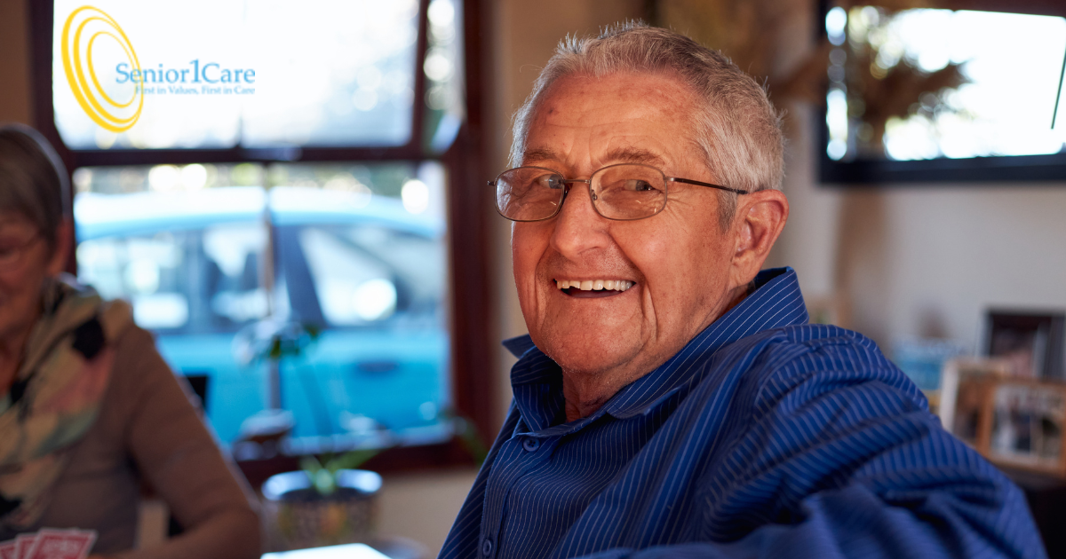 Happy, smiling senior man sitting at a table and looking over his shoulder.