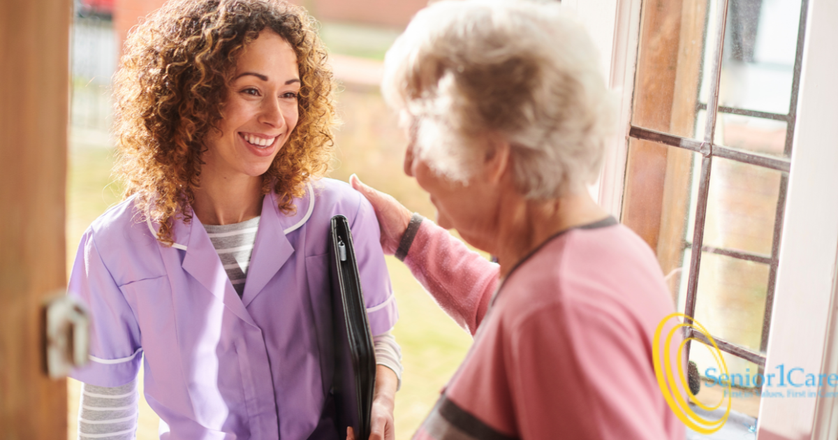 Smiling senior stands at the front door and welcomes a new caregiver into her home