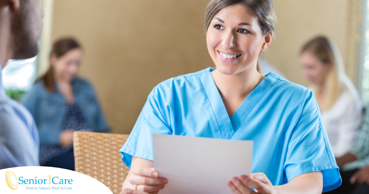 A woman in scrubs holds a paper while interviewing with someone else, representing how a solid caregiver resume can get you to an interview.