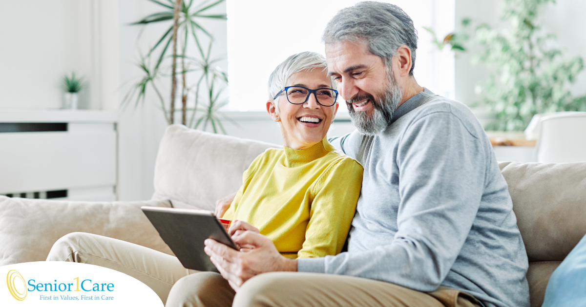 A senior couple smiles while looking at a laptop, showing how online resources can help family caregivers.