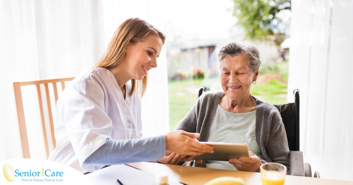 A professional caregiver smiles as she helps a happy senior client with her tablet, showing that she is managing caregiving stress well.