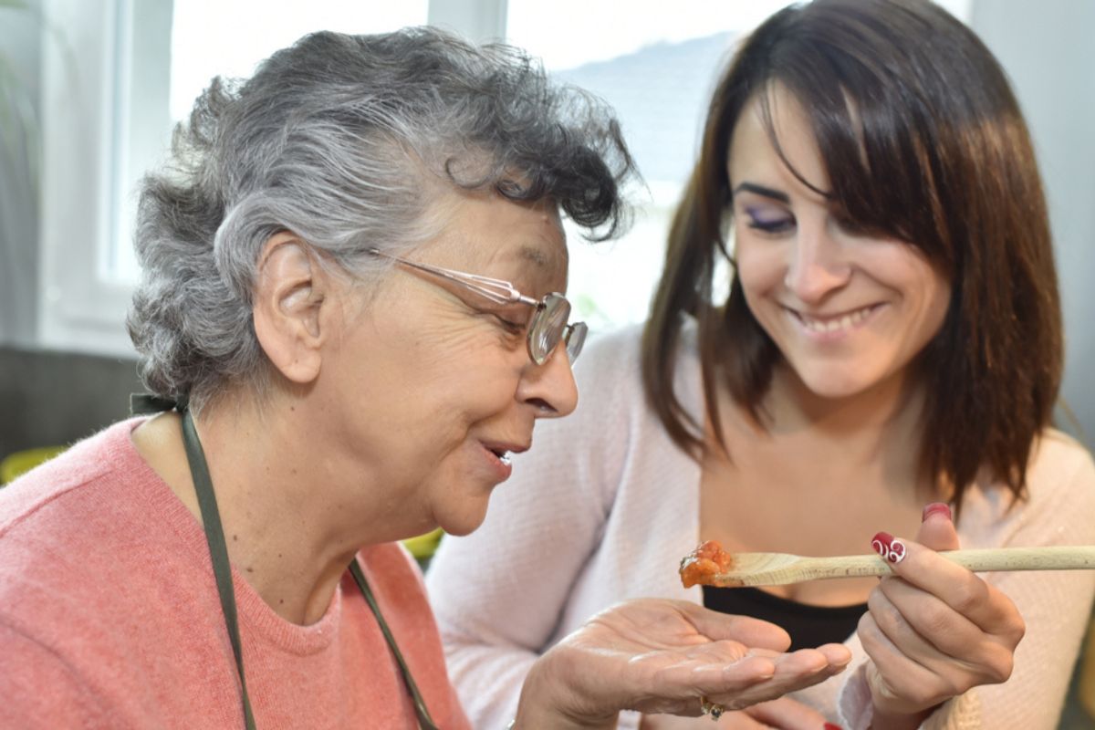 MealPlanningWarsaw2 A caregiver helps an elderly woman with meals, feeding her some food on a wooden spoon. Meal planning in Warsaw.