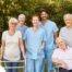 2 caregivers and seniors smile while in a group representing how caregivers can facilitate socialization.