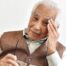 An older adult holds his head and his glasses representing vision problems like macular degeneration.