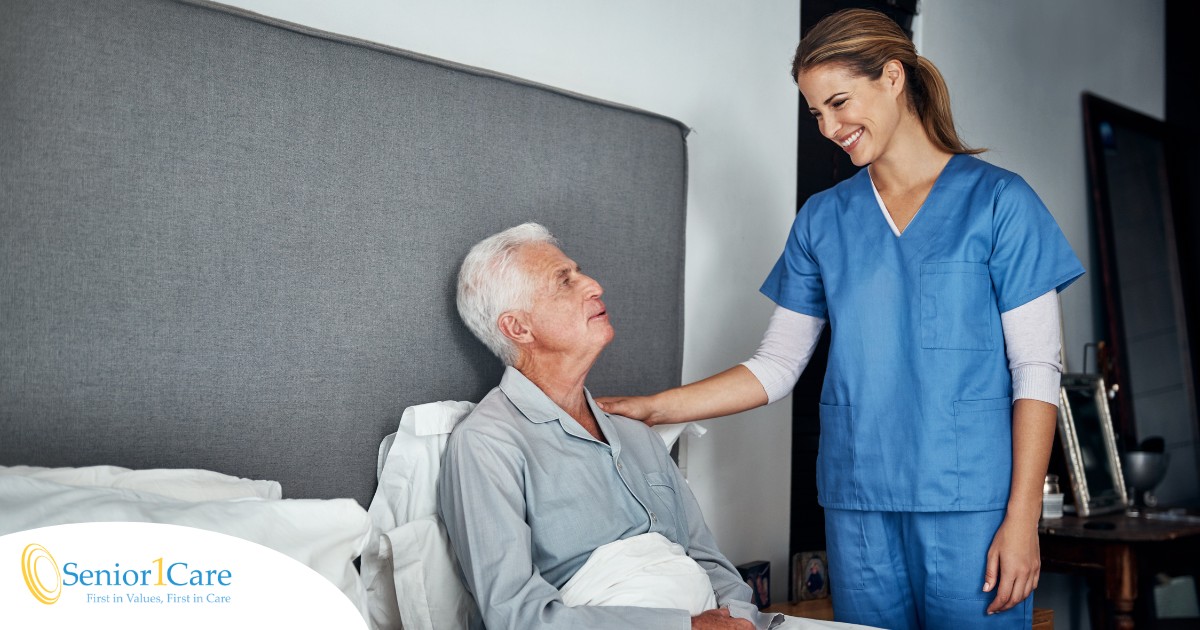 A caregiver smiles at an older client in bed, representing the compassion involved in being a live-in caregiver.