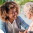 A caregiver smiles at an older client in a chair, representing the joy that can come from a healthy work-life balance.
