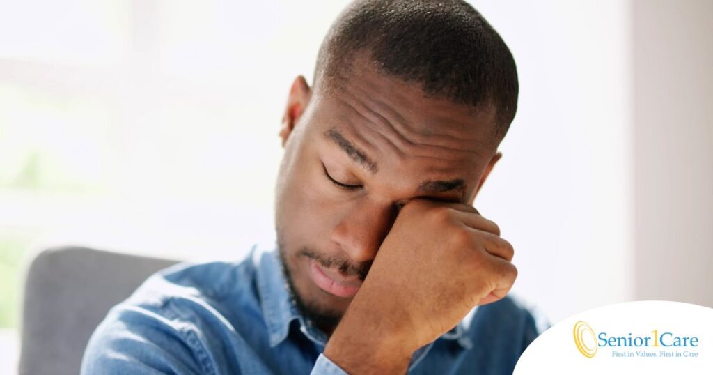 A man tiredly rubs his eyes, representing the exhaustion that can come with family caregiving.