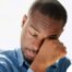 A man tiredly rubs his eyes, representing the exhaustion that can come with family caregiving.