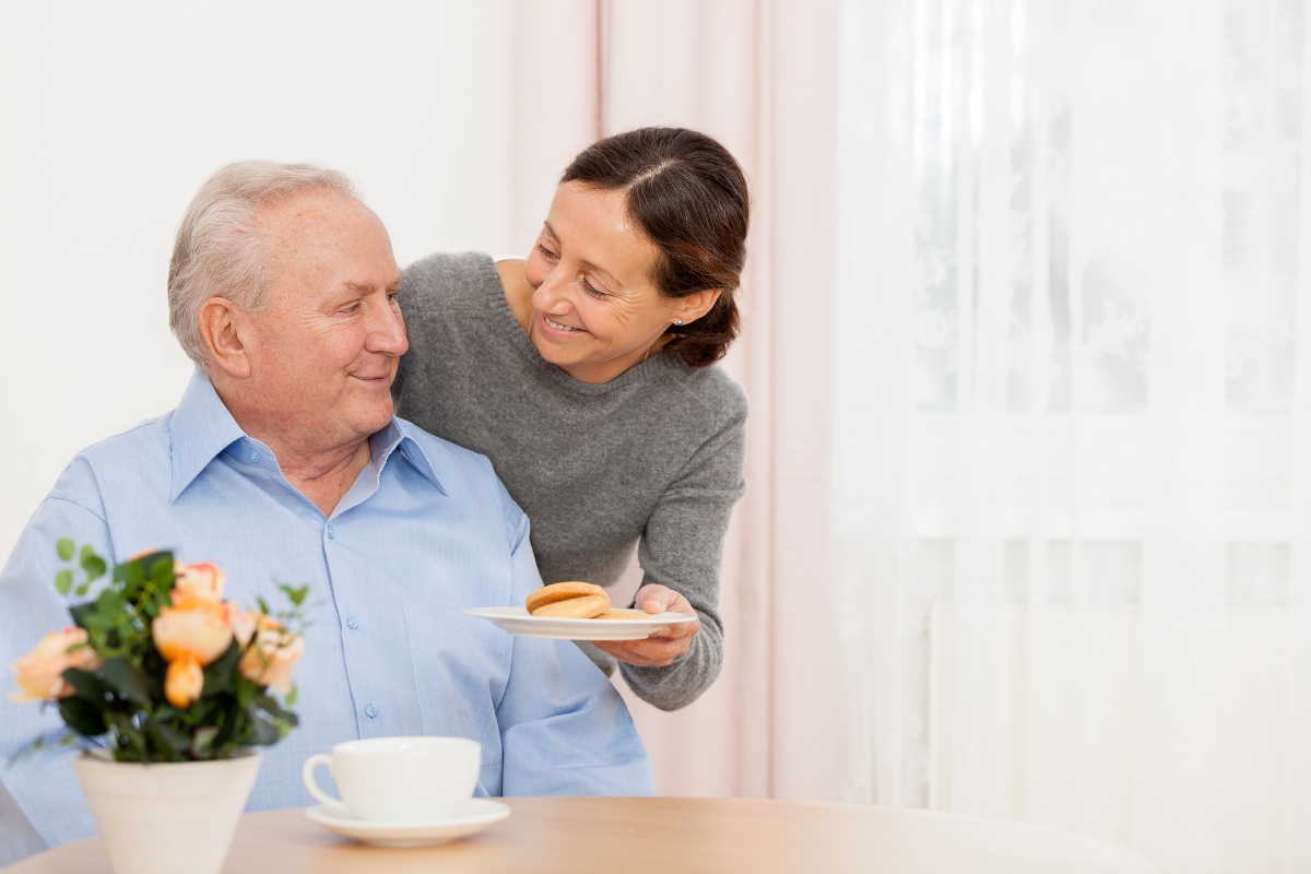 Senior1Care caregiver offering a meal to an elderly man at home in Goshen, providing compassionate meal planning and support.
