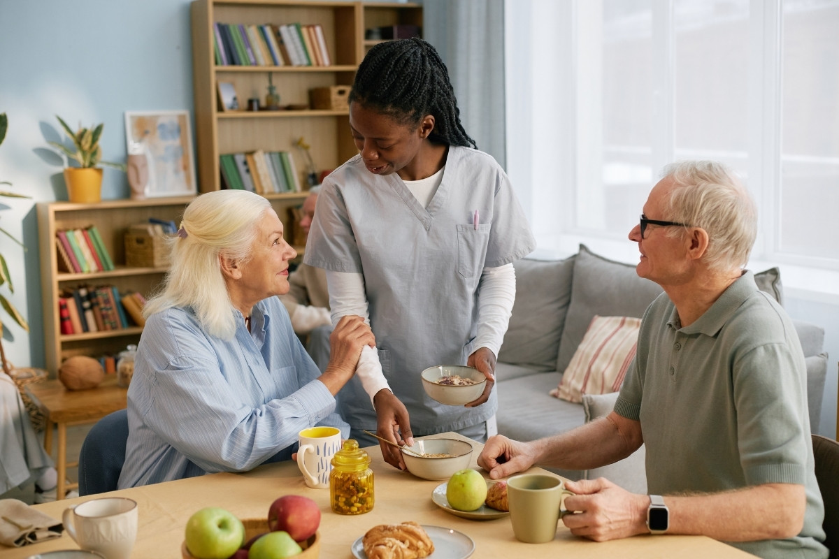 Heartwarming Meal Planning in Carmel A compassionate caregiver serving a nourishing breakfast to an older couple sitting at their home dining table, representing thoughtful Meal Planning in Carmel.