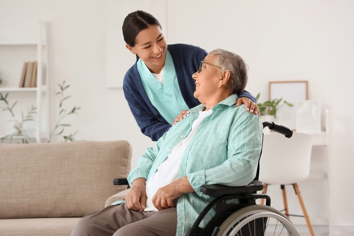 Compassionate Caregiver Providing Supportive Recovery Care in Carmel A comforting caregiver resting a gentle hand on the shoulder of a smiling older woman seated in a wheelchair, illustrating compassionate Recovery Care in Carmel.