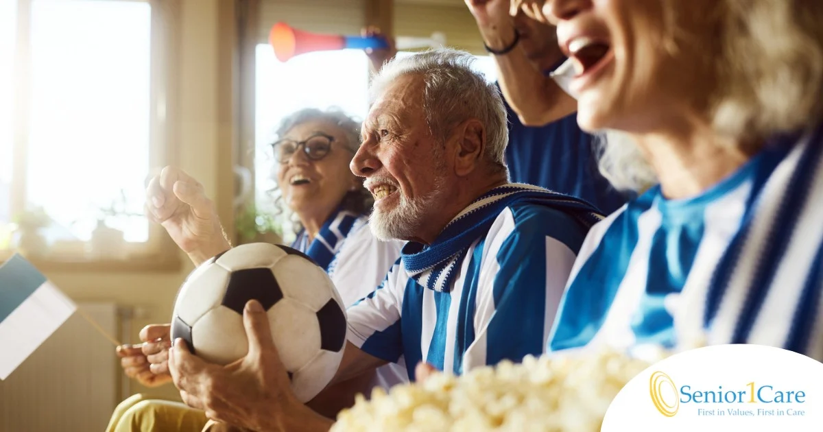 A group of joyful seniors in blue and white jerseys cheering during a World Cup match, illustrating the power of human connection fostered by Senior1Care.
